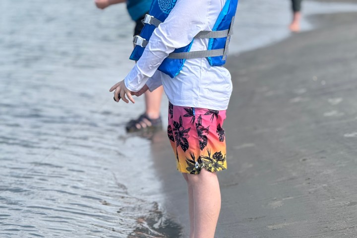 Person in blue hat and life vest stands at the shoreline, with two people in the background.
