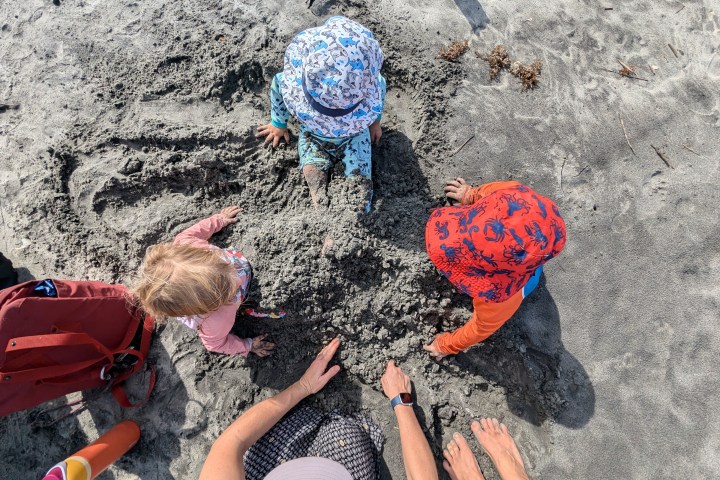 Three children and one adult playing in sand on a beach.