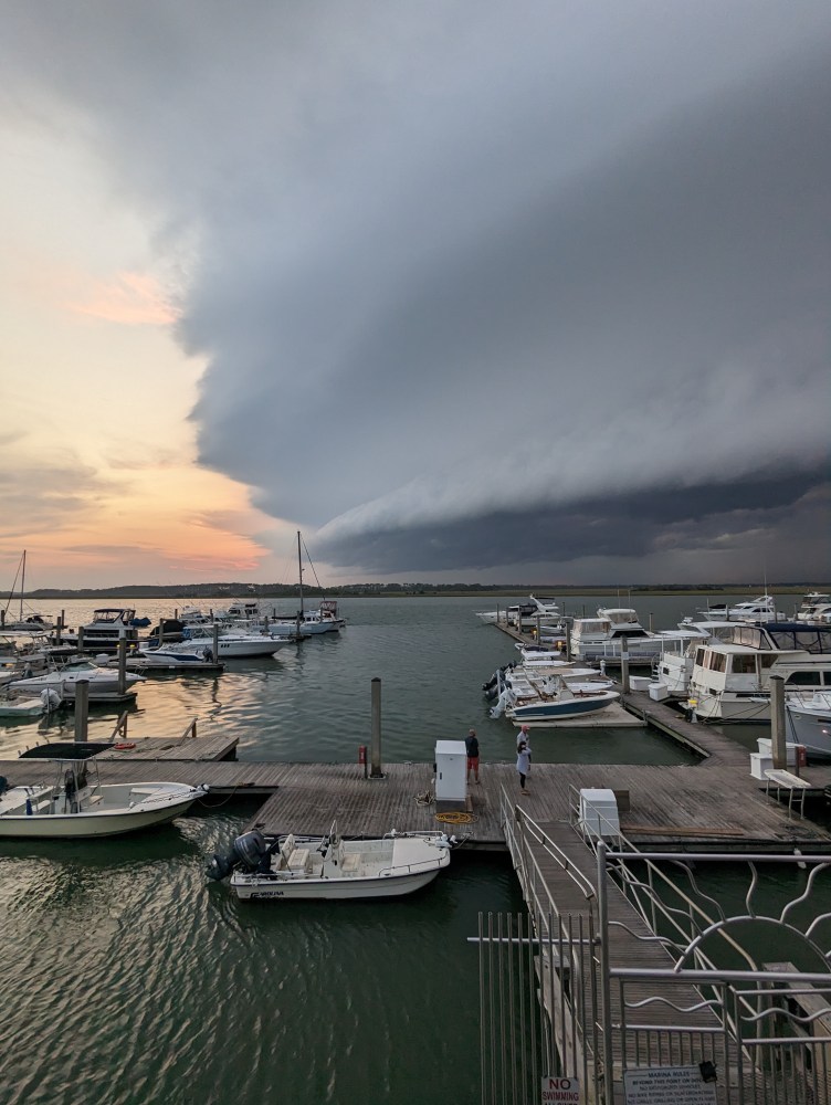 Marina with boats under a dramatic sky, dark storm clouds approaching from the right.