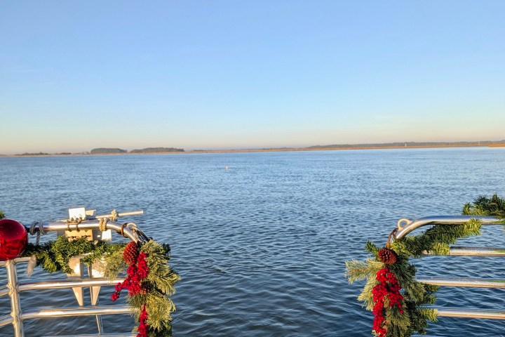 Dock with festive garlands overlooking calm water under clear blue sky.