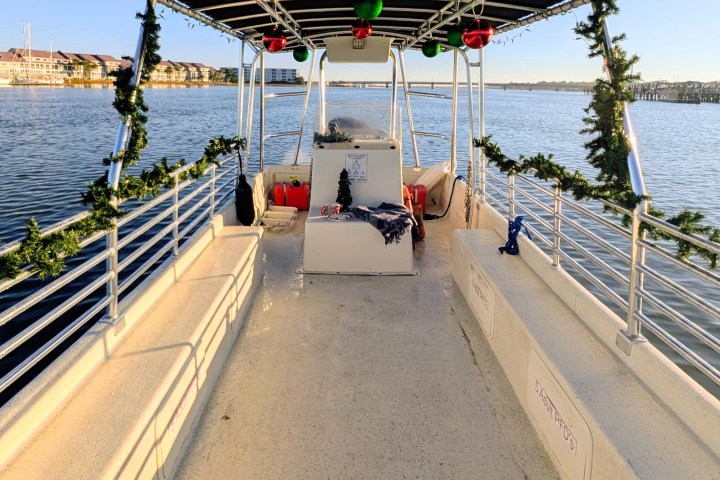Boat deck decorated with holiday garlands and ornaments, docked on calm water.