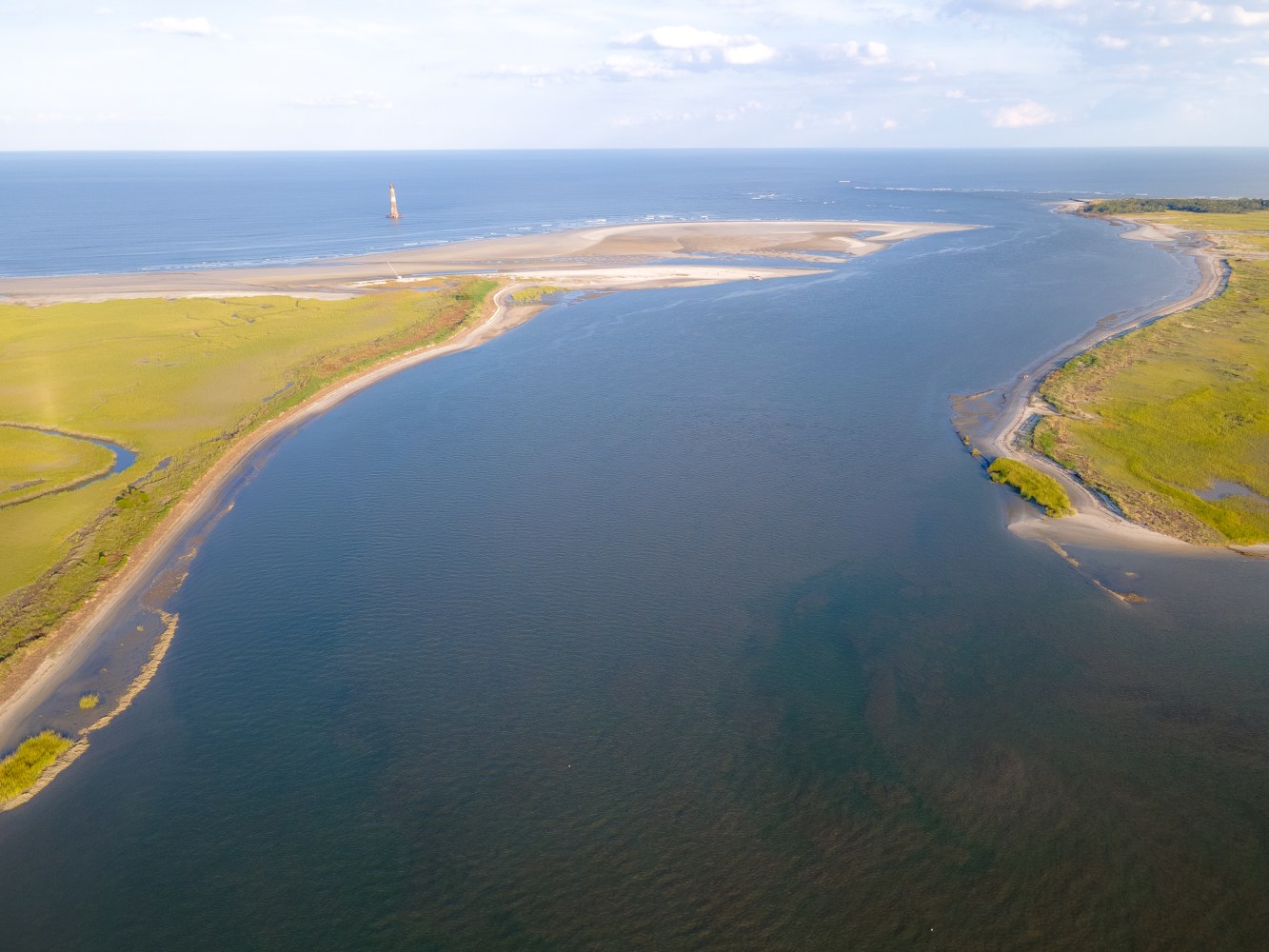 Aerial view of a river meeting the ocean with grassy banks and sandy beach.