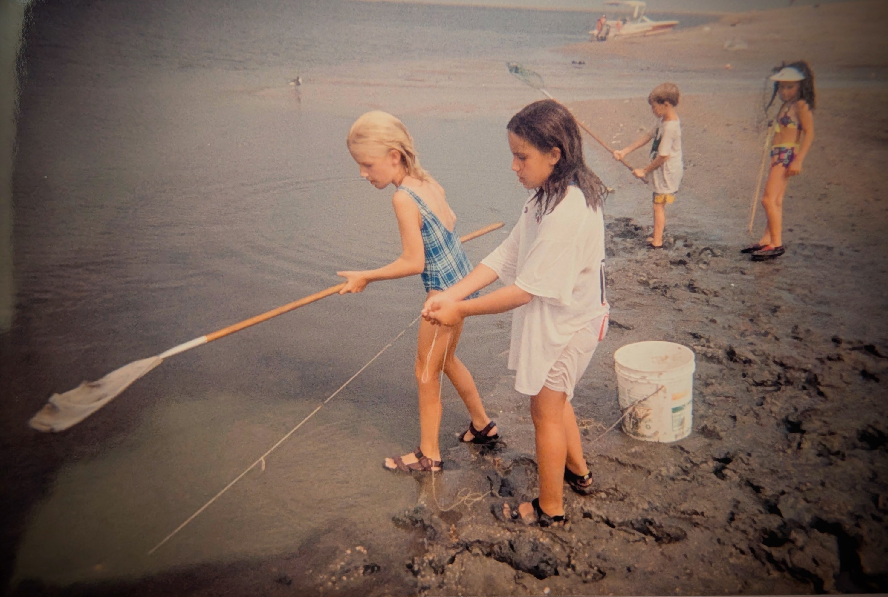 Kids using nets to fish on a sandy lakeshore.