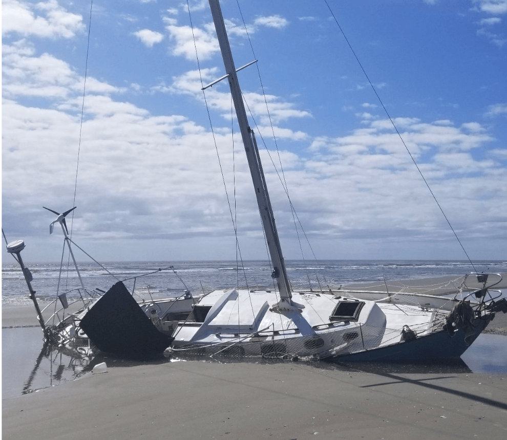 Beached sailboat on sandy shore under a cloudy sky.
